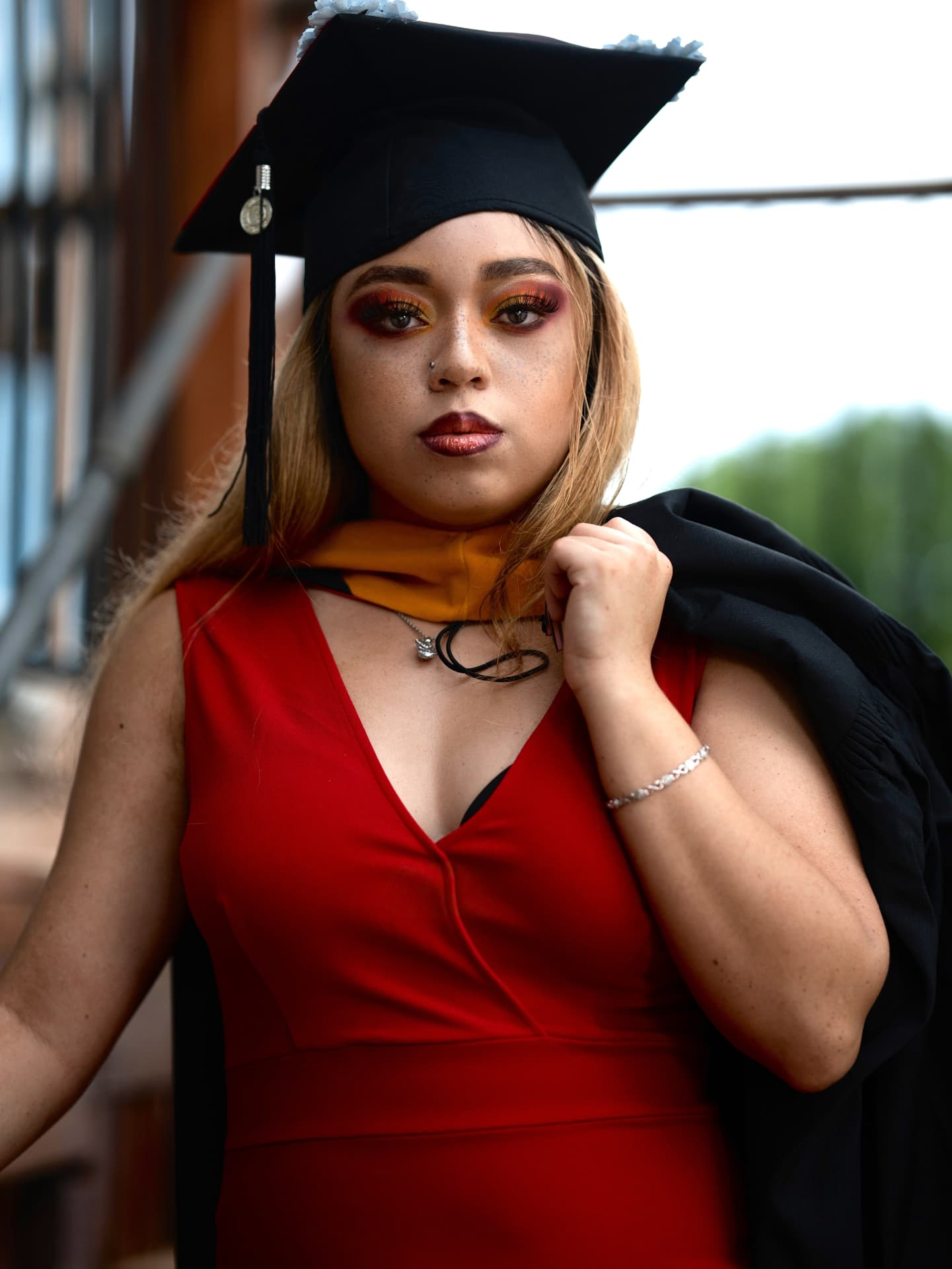 Graduate in cap and gown with a red dress and gold stole